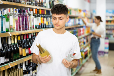 Teenager hält im Supermarkt eine Flasche Wodka und Champagner in der Hand.